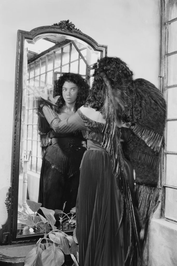 Leonor Fini, artista, si specchia indossando ali che la fanno somigliare a una delle sfingi che ha ritratto